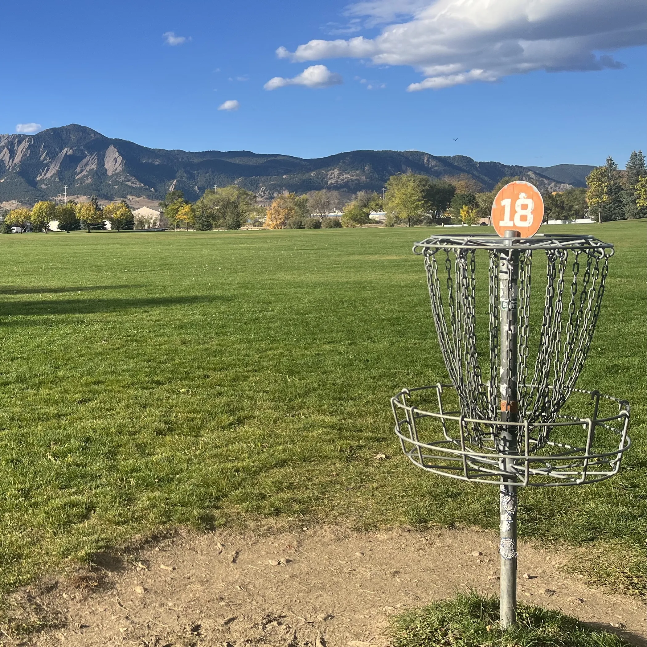 A disc golf basket with a lake and mountains in the background at Valmont Disc Golf Course in Boulder, Colorado
