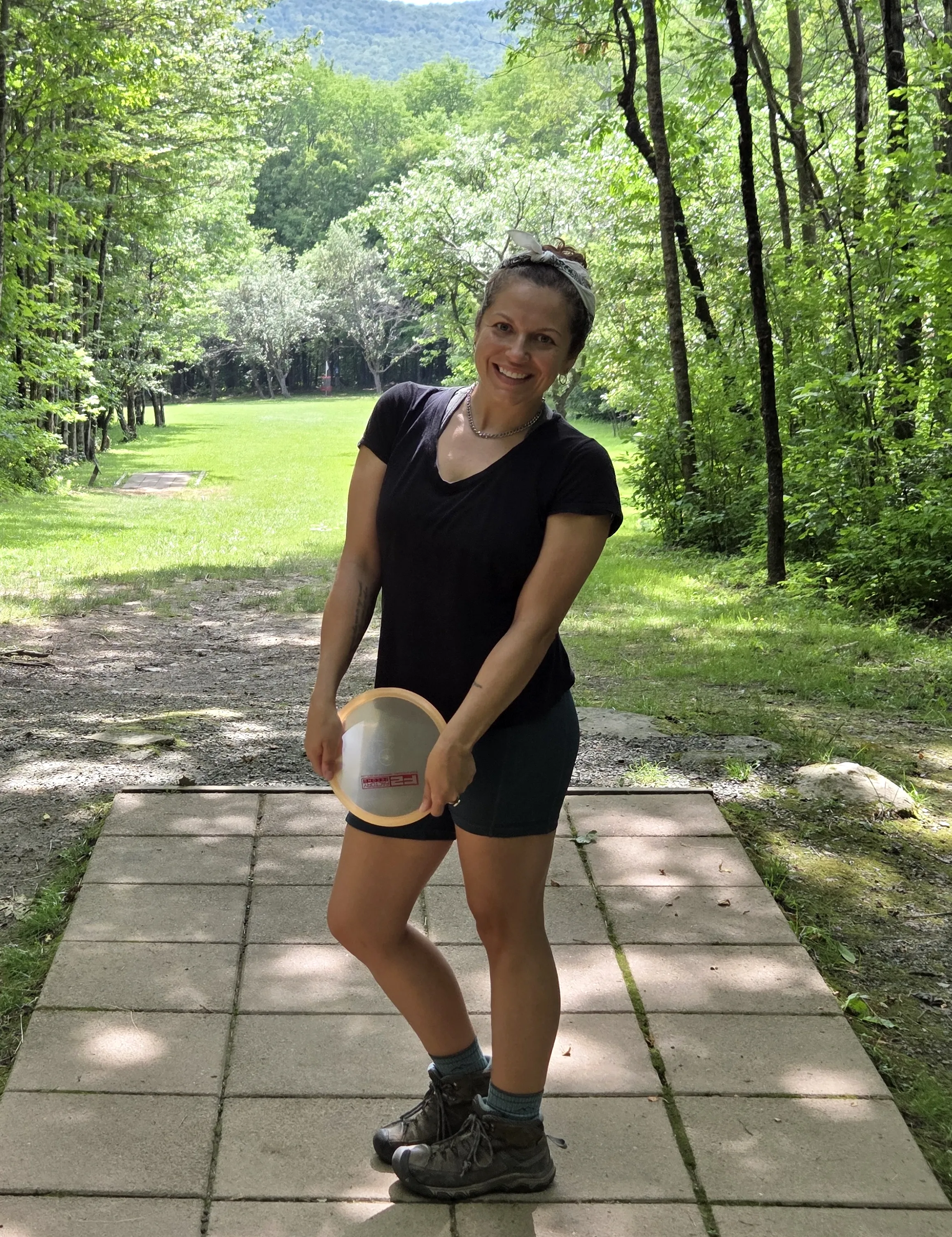 Monique holding a disc on a disc golf tee pad